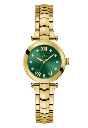 Kuldtooni kell, millel on ümmargune roheline kellaseier, Rooma numbrid, diamanthakaste sarnased markerid ja linkmetallist käevõru. Külgedel on kroon.