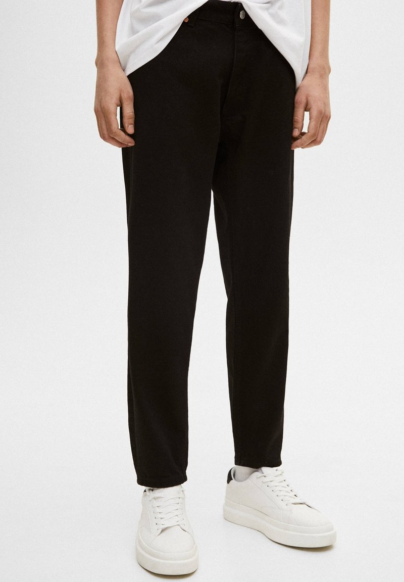 Czarne spodnie o prostym kroju i prostym designie, wykonane z bawełny. Połączone z białymi trampkami o fakturowanej powierzchni.