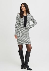 Sorte og hvide houndstooth-mønstrede jakkesæt med en cropped blazer og tætsiddende nederdel; parret med knæhøje sorte støvler.