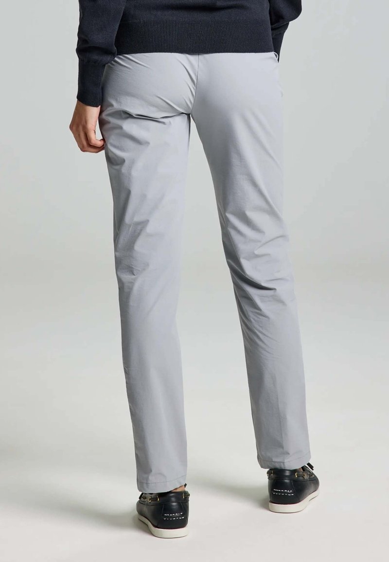 Pantalons gris clair avec une coupe droite, en tissu lisse. Chaussures noires avec semelle blanche, vues de derrière.
