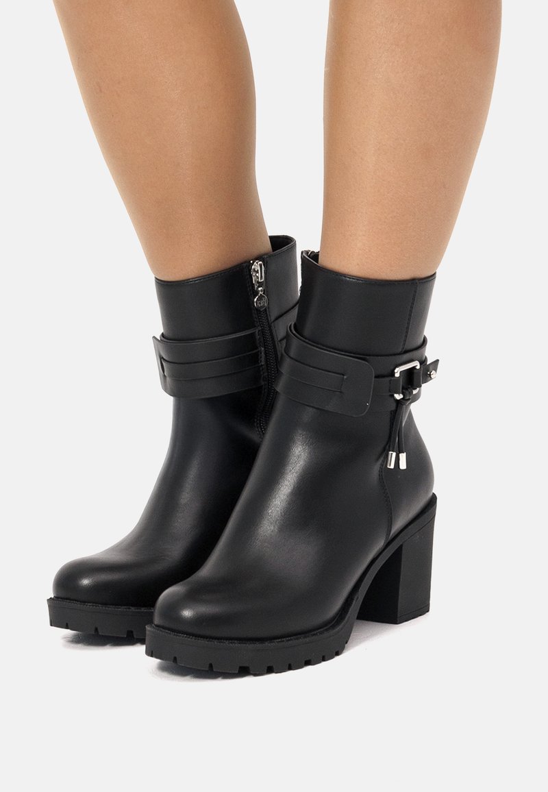 Botas de tobillo de cuero negro con tacón ancho, que cuentan con un cierre lateral, acentos de correa y una suela texturizada para mayor agarre.