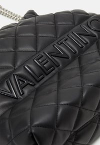 Černá prošívaná kožená kabelka s velkým embosovaným logem Valentino a stříbrným řetízkovým popruhem.