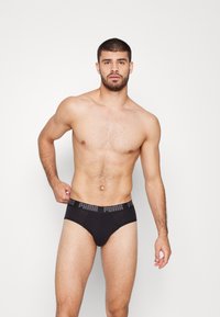 Schwarze Baumwollunterhose mit einem Logo-Bund, klassischer Schnitt und glatter Textur. Das Modell ist männlich, hat kurzes Haar und einen muskulösen Körperbau.