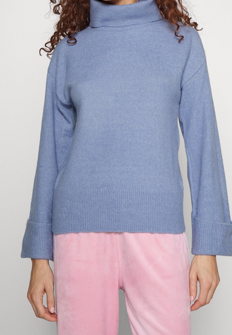 Světle modrý pletený rolák s ribovanou strukturou a širokými rukávy, spárovaný s měkkými růžovými kalhotami.