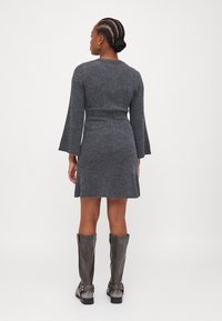 Robe tricotée grise côtelée avec de longues manches évasées, taille cintrée et jupe évasée. Associée à des bottes en cuir grises montantes.