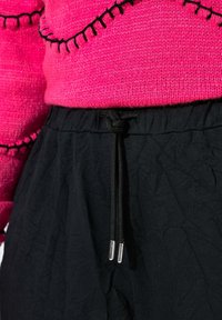 Różowy sweter z dzianiny z czarnymi frędzlami w połączeniu z czarnymi spodniami o teksturowanej fakturze, posiadającymi elastyczny pas ze sznurkiem i srebrnymi końcówkami.