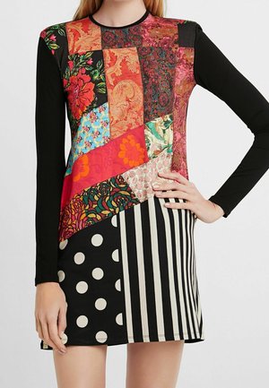 Langärmliges Kleid mit schwarzen Ärmeln und einem mehrfarbigen Patchwork-Oberteil mit Blumen-, Streifen- und Punktenmuster am Rock.