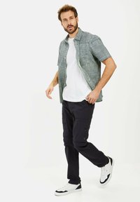 Korte mouw gestreept shirt in groen en wit, witte T-shirt eronder, navy cargo pants en witte sneakers met donkerblauwe accenten.
