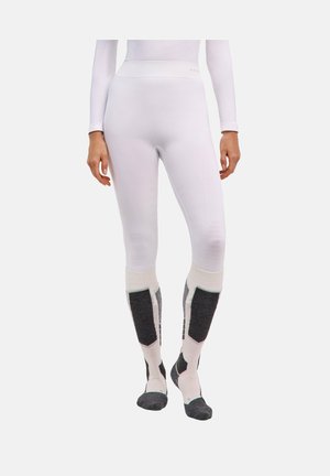 Kobieta ubrana w dopasowane białe legginsy i białe skarpetki do kolan w czarno-biały wzór, stojąca na jednolitym tle.