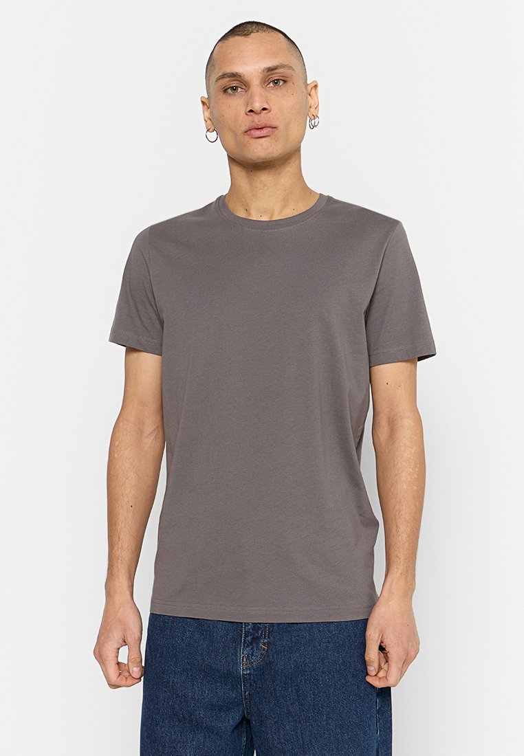 T-shirt grigio in cotone con collo rotondo e maniche corte, caratterizzato da una vestibilità comoda e una texture liscia, abbinato a jeans in denim scuro.