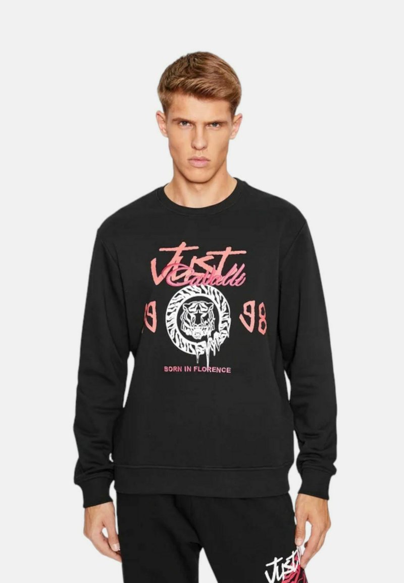 Felpa nera con una grande grafica bianca e rosa di una testa di leone, testo "JUST CAVALLI" e "BORN IN FLORENCE", polsini e orlo a coste.