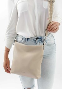 Borsa a tracolla in pelle beige con superficie testurizzata, tracolla regolabile a motivo e finiture in argento. Design minimalista con branding discreto.