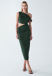 Asymmetrische groene jurk van zachte stof, met een uitsparing in de taille, geplooide details en een midilengte rok.