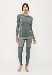 Conjunto atlético de estampado verde que incluye una camiseta de manga larga con diversas texturas y diseños, emparejada con leggings ajustados a rayas.