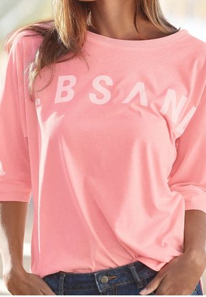 Pink short-sleeve shirt made of soft fabric. Features oversized fit, boat neck, and white graphic text across the chest.