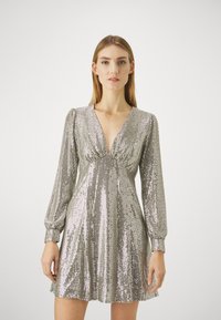Robe en sequins argentés avec un décolleté en V, des manches longues et un détail froncé à la taille ; longueur genou avec une jupe fluide.