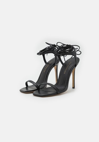 Sandalias de tacón alto negras con un diseño elegante, que presentan tiras delgadas, puntera cuadrada y detalles de cordones en el tobillo.