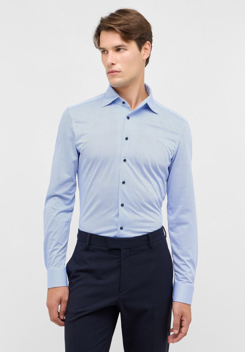 Camicia azzurro chiaro con motivo, maniche lunghe, colletto a bottoni e bottoni scuri. Abbinata a pantaloni scuri per un look formale.