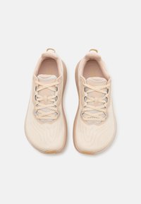 Scarpe da ginnastica beige con upper testurizzato, dettagli in mesh e lacci tondi. Presentano uno schema ondulato sottile sul materiale e suola in gomma.