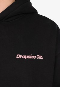 Black hoodie with pink embroidered text "Dropsize Clo." on the chest, showing upper torso and part of the hood.
