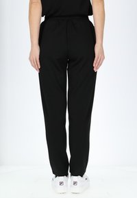 Zwarte taps toelopende joggers met een elastische tailleband, gemaakt van zacht materiaal, gecombineerd met witte stevige sneakers met een logoprint.