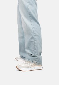 Witte sneakers met een textuur van gaas en beige accenten, gecombineerd met lichtblauwe, ruime jeans met onafgewerkte zomen en een losse pasvorm.