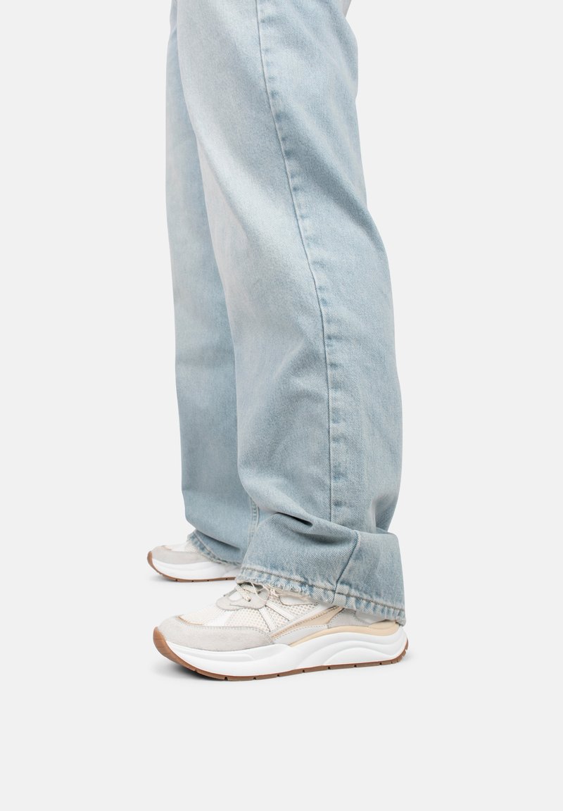 Witte sneakers met een textuur van gaas en beige accenten, gecombineerd met lichtblauwe, ruime jeans met onafgewerkte zomen en een losse pasvorm.