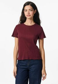 Burgundy t-shirt med korta ärmar och ribbat mönster, med rundad halsringning och vågiga kanter på ärmar och nederkant. Kombinerad med jeans.