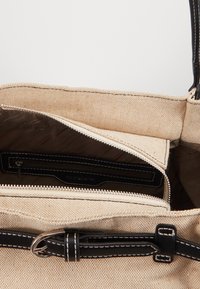 Canvas toteväska med en beige utsida, svarta läderdetaljer och ett dragkedjeförsett innerfack. Har sömnadsdetaljer och etikett från U.S. Polo Assn.