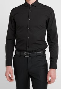 Zwart overhemd met lange mouwen, slim fit, knoopsluiting aan de voorkant, zachte textuur, gecombineerd met een zwarte riem en broek.