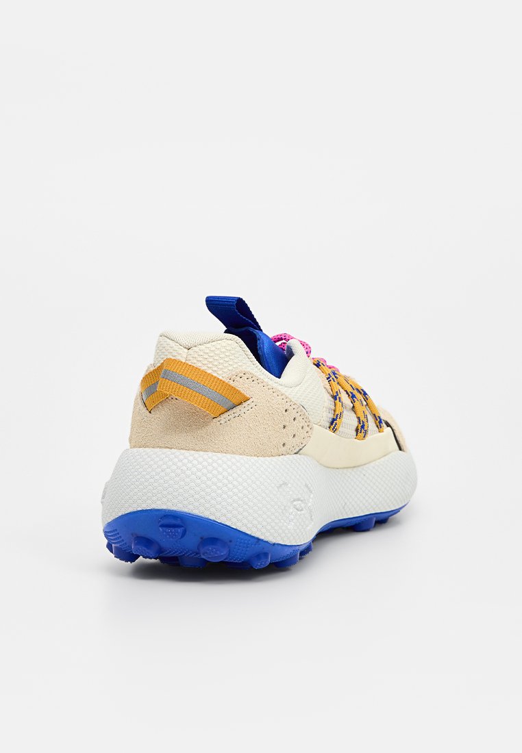 Zapatillas con una parte superior crema, detalles texturizados en beige, suela azul y cordones multicolores. Presentan una pestaña en el talón y un diseño a rayas en el lado.