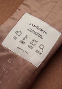 Brązowy materiał z metką zawierającą ikony wskazujące na mieszankę wełny, komfort termiczny, elastyczny materiał oraz dbałość o szczegóły.