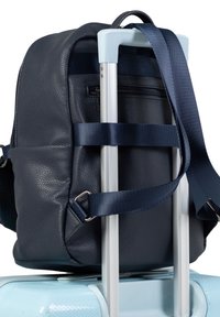 Sac à dos en cuir texturé bleu marine fixé sur une valise en aluminium, doté d'une poignée de transport supérieure et de sangles en tissu ajustables.