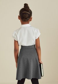 Weiße kurzärmlige Bluse mit Kragen und grauem, schwingendem Rock. Das Outfit wird mit schwarzen Leggings kombiniert, und das Kind hält ein Buch in der Hand.