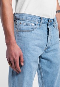 Jeans in denim azzurro chiaro con un taglio dritto, cinque tasche e hardware in metallo. Il tessuto ha una consistenza morbida e una minimale sbiaditura.