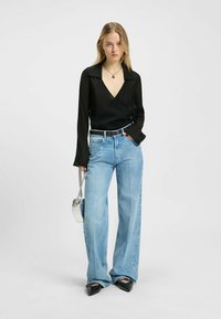 Sort langærmet omslagstop med V-hals, parret med lyseblå bredbenede jeans og sorte spidse sko. Sølv kædebagt.