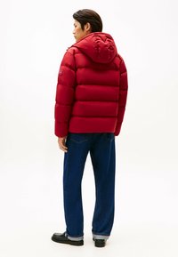 Rød pufferjakke med hætte, der har quiltede sektioner. Sammen med løstsiddende blå jeans og sorte loafers.