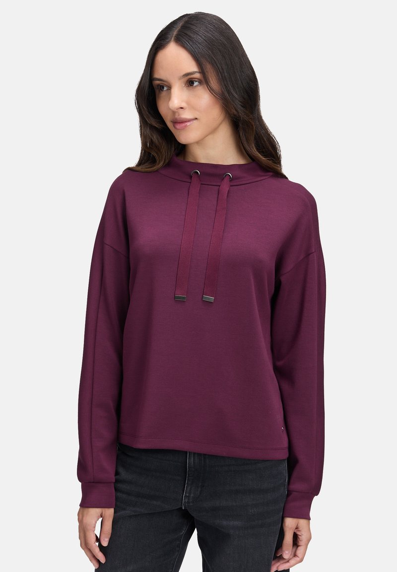 Bordowy sweter z wysokim kołnierzem, sznurkami i długimi rękawami; wykonany z miękkiej tkaniny o gładkiej fakturze; charakteryzuje się luźnym krojem.