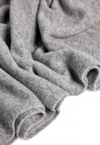 Tissu en tricot gris avec une apparence douce et texturée, présentant des plis délicats et un tomber léger. Fini lisse et profondeur subtile.