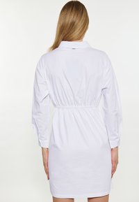 Weißes Hemdkleid mit langen Ärmeln, Kragenhals, gerafftem Taillenbereich und geknöpften Manschetten. Glattes Material mit dezentem Glanz.