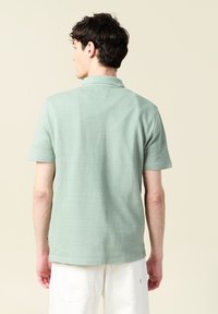 Paita polo vaaleanvihreänä, lyhyet hihat, textured-kangasta hienovaraisella kuviolla, klassinen kaulus ja pieni sivulogo. 