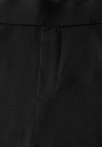 Tessuto nero con una consistenza liscia e una leggera lucentezza. Presenta una tasca laterale e una cintura cucita. Vista ravvicinata che evidenzia i dettagli.