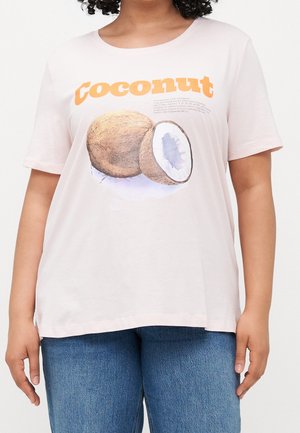 Woman wearing light pink T-shirt with orange "coconut" text and coconut illustration, paired with blue jeans, standing against white background.