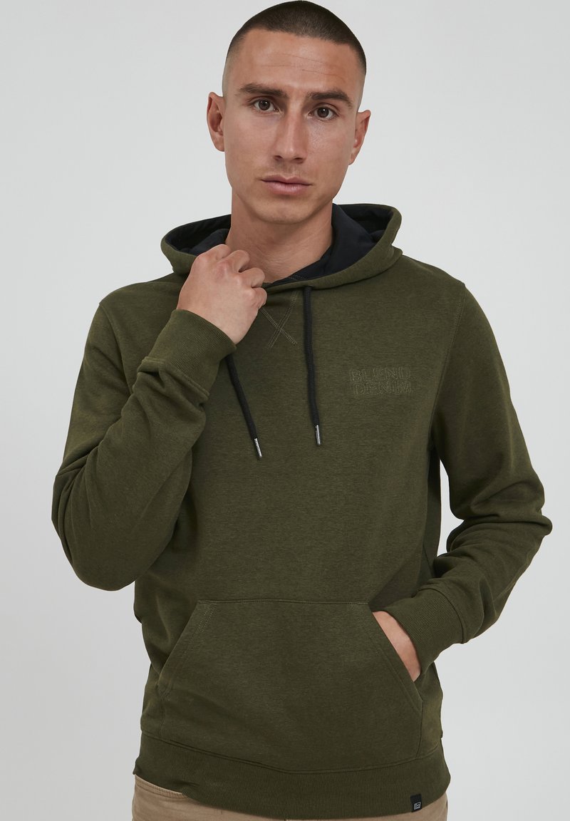 Olivgrüner Hoodie aus weichem Stoff, mit einer vorderen Tasche, schwarzen Kordeln und dezentem Branding auf der Brust.