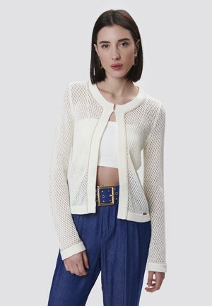 Cardigan blanc tricoté avec un design en mesh, un col rond et des manches longues. Associé à un pantalon bleu taille haute et une ceinture avec des accents dorés.