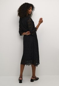 Black lace dress with a scalloped hem, side slits, and three-quarter sleeves, featuring a floral pattern and a relaxed fit.