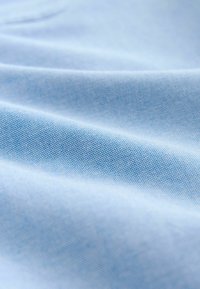 Svetlo modra tkanina z gladko teksturo, ki vsebuje subtilne vzorce pik. Površina prikazuje nežne gube in zavoje.