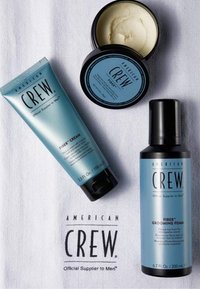 American Crew haarstylingsproducten, waaronder een tube fibercrème, een open pot fibercrème en een fles fiber grooming schuim op een witte doek.