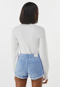 White ribbed sweater with long sleeves, paired with light blue high-waisted denim shorts featuring rolled cuffs and two back pockets.