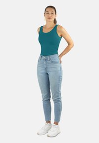 Türkise Tanktop, hochgeschnittene hellblaue Jeans und weiße Sneakers. Der Stoff ist glatt; die Jeans haben eine klassische Passform mit Fronttaschen.